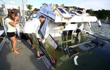 Sepasang suami istri melihat kapal yang rusak di marina di Tutukaka, Selandia Baru, Minggu, (16/1/2022), setelah gelombang dari letusan gunung berapi menyapu marina. Sebuah gunung berapi bawah laut meletus dengan cara yang spektakuler Sabtu di dekat negara Pasifik Tonga, mengirimkan gelombang tsunami menerjang pantai dan orang-orang bergegas ke tempat yang lebih tinggi. 