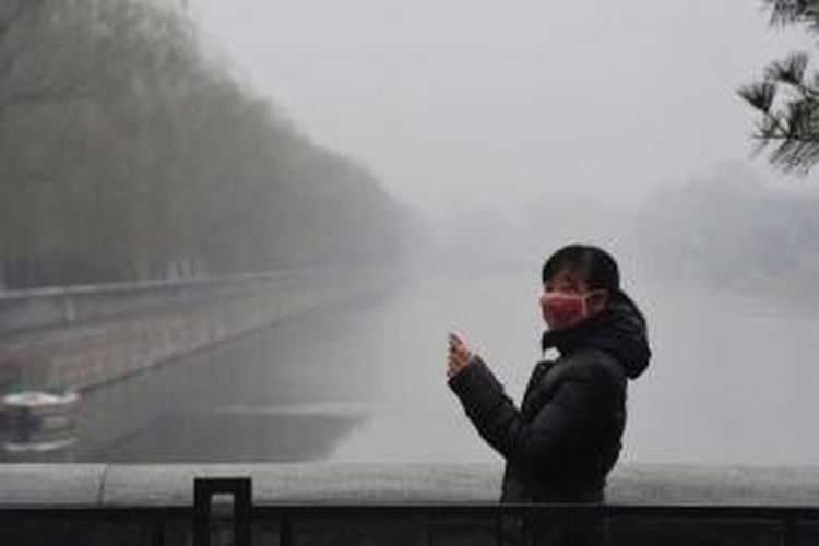 Seorang wanita mengenakan masker wajah saat mengambil foto di sekitar Forbidden City yang diselimuti oleh kabut asap polusi udara, Selasa, 8 Desember 2015. Pemerintah Kota Beijing, Senin sore, untuk pertama kalinya dalam sejarah menaikan status kabut menjadi darurat berstatus ?berwarna merah? yang merupakan status darurat paling tinggi.