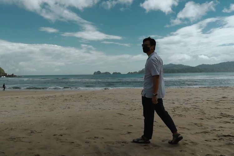 Dion Wiyoko ketika berwisata mengenakan masker di pantai Pulau Merah, Banyuwangi, Jawa Timur.