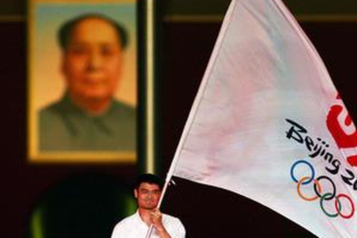 Bintang NBA Yao Ming memegang bendera Olimpiade untuk memandai hitungan mundur satu tahun Olimpiade Beijing pada 8 Agustus 2007. Di latar belakangnya ada poster besar Ketua Mao.