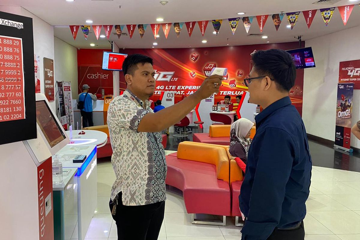 Staf gerai Grapari Telkomsel memeriksa suhu pengunjung