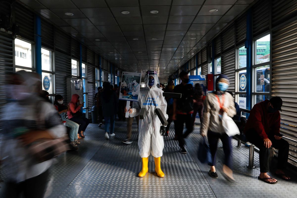 Maskot Manusia Covid membawa poster bertulisakan data penderita Covid-19 terlihat di Halte Transjakarta Harmoni, Kamis (16/7/2020). Maskot Manusia Covid bertujuan mengingatkan penumpang Transjakarta untuk disiplin mematuhi prosedur kesehatan selama masa PSBB Transisi Tahap II berlangsung.