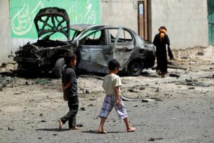 Beberapa anak berjalan melintasi bangkai mobil pembawa bom yang hancur setelah meledak di dekat sebuah masjid Syiah di ibu kota Yaman, Sana'a, Rabu (17/6/2015).