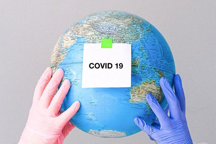 An image of two hands holding globe with a sticker saying Covid-19. 