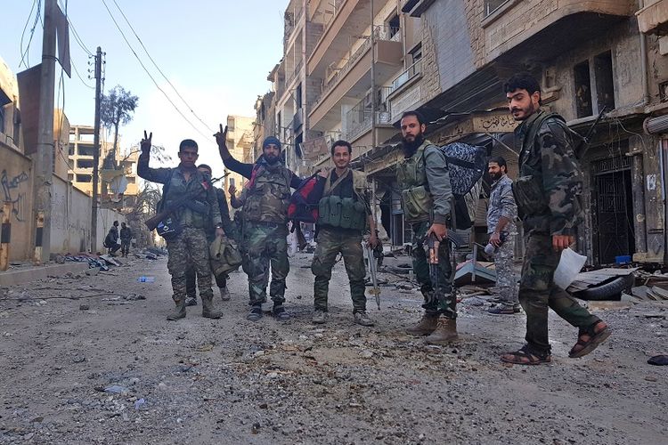 Para prajurit AD Suriah dan milisi pro-pemerintah berfoto di depan sebuah gedung yang rusak berat di kota Deir Ezzor pada 3 November 2017. 