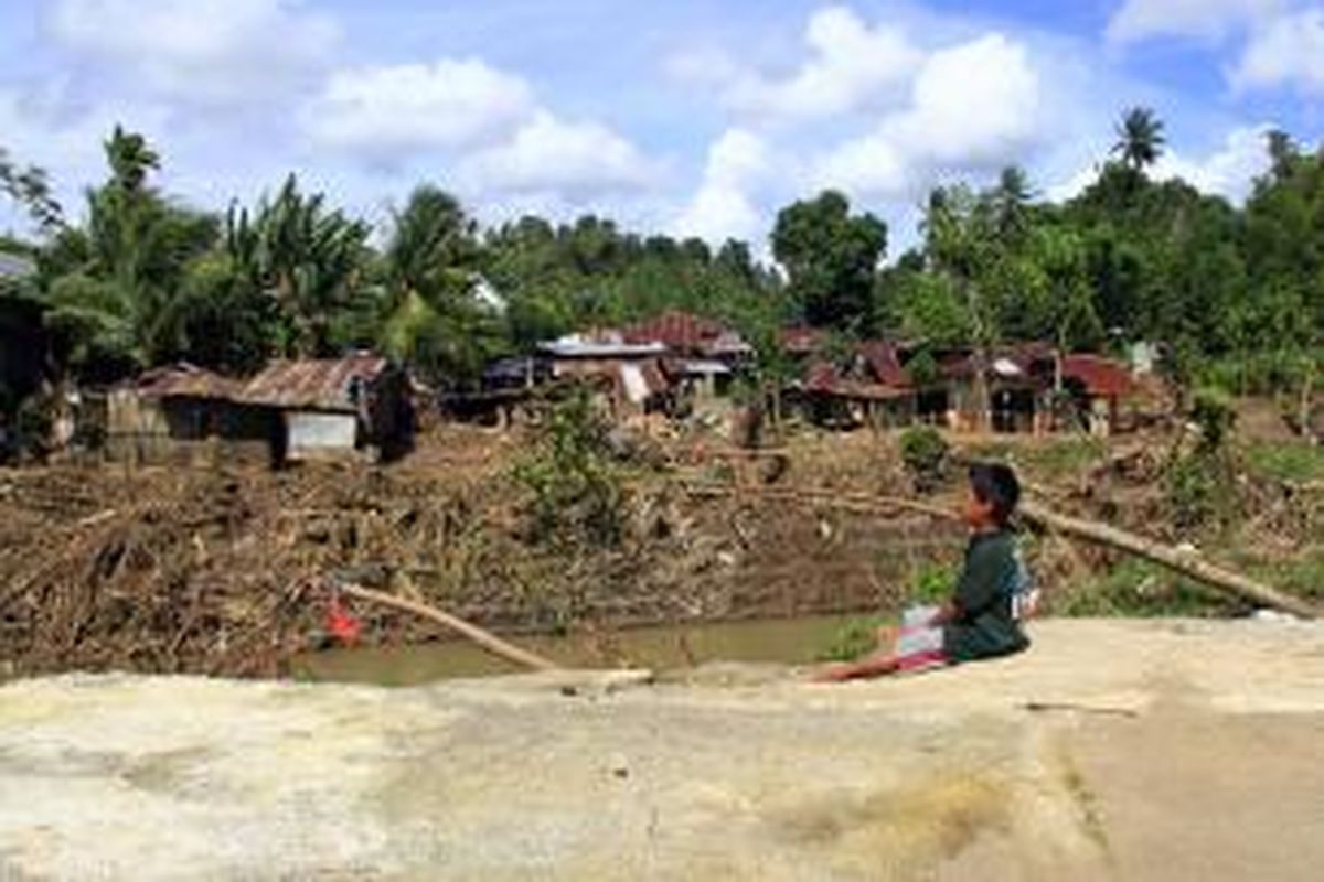 Brain (9), warga Tikela, Minahasa duduk di bekas rumahnya yang hanyut tersapu banjir bandang.