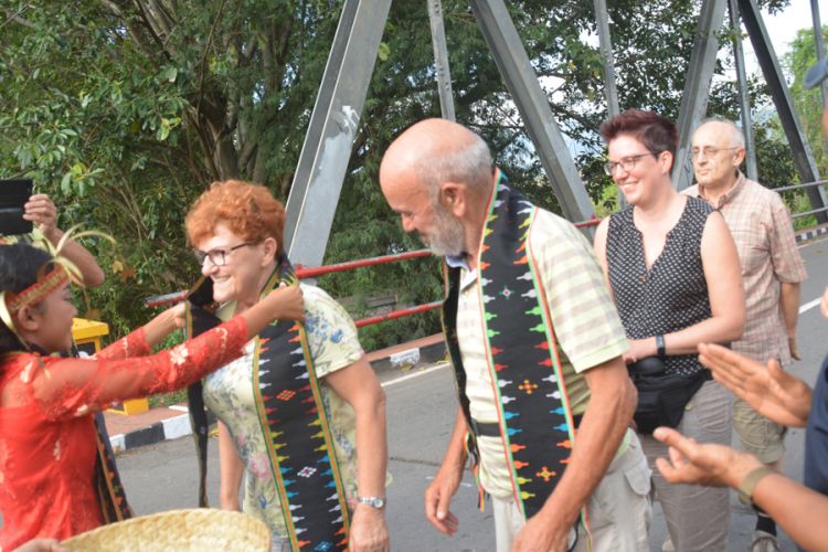 Seorang siswi SMPK Waemokel mengalungkan tamu Italia dan Jerman dengan selendang Songke di Jembatan Waemokel, Kabupaten Manggarai Timur, NTT, Rabu (15/8/2018).