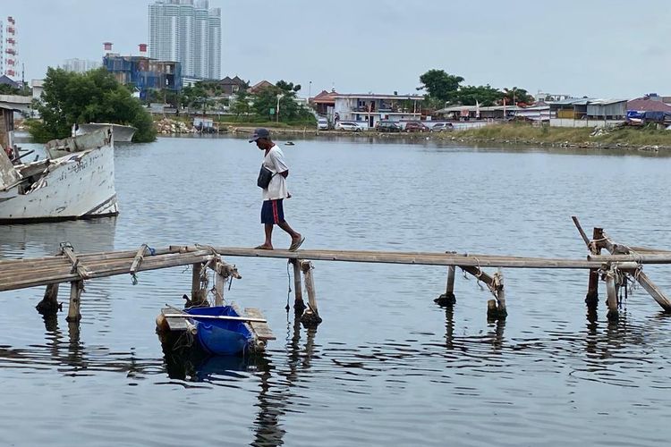 Seorang warga melewati jembatan bambu untuk menyebrang dari Kampung Pojok, Muara Baru, Penjaringan, Jakarta Utara, Jumat (27/1/2023). Kampung ini berada di sisi Teluk Jakarta, yang dibangun dengan fondasi bambu serta papan seadanya. 