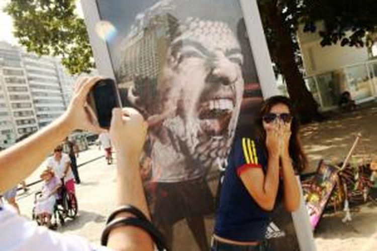 Seorang suporter Spanyol berpose di depan papan reklame bergambar Luis Suarez di Pantai Copacabana, Rio de Janeiro, Brasil. 