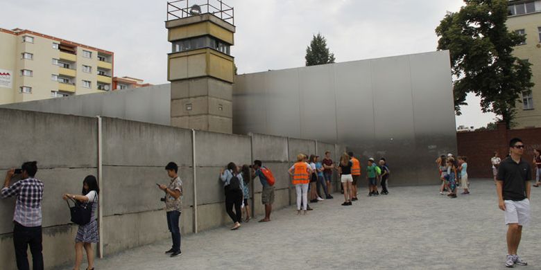 Wisatawan mengintip dari celah-celah tembok di Berlin Memorial Wall, Rabu (21/6/2018), untuk membayangkan bagaimana korban yang tewas saat melarikan diri melewati Tembok Berlin.