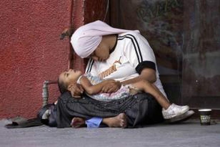 Seorang wanita pengungsi Suriah memegang anaknya saat mereka tertidur di trotoar sebuah jalan di Sidon, sebuah kota di selatan Lebanon, 18 Juli 2013. Eksodus pengungsi Suriah kian banyak dalam beberapa bulan terakhir.
