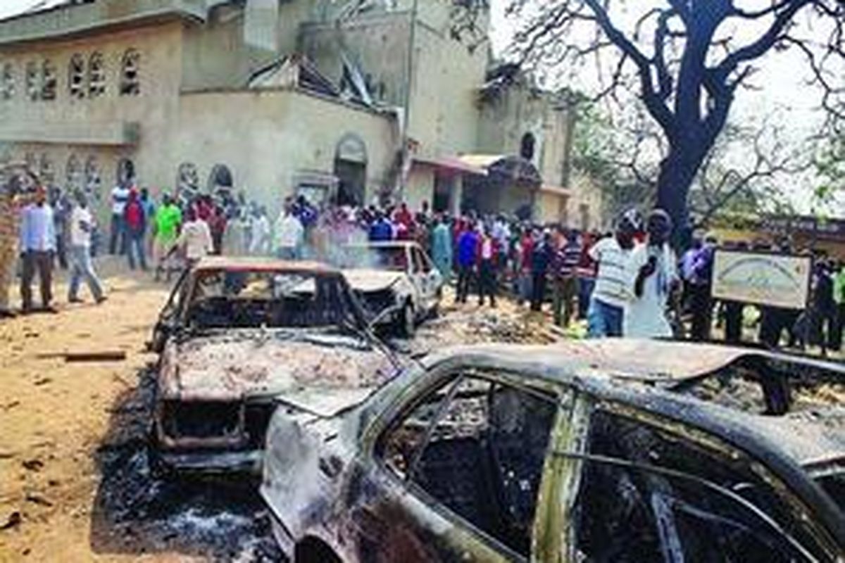 Warga berkumpul di sekitar bangkai-bangkai mobil yang hangus terbakar di lokasi ledakan bom di Gereja Katolik St Theresa di Madalla, Nigeria, Minggu (25/12). Bom meledak saat diadakan misa Natal di beberapa gereja di Nigeria, menewaskan sedikitnya 39 orang. Sekte Islam radikal Boko Haram mengklaim bertanggung jawab terhadap serangan bom tersebut.