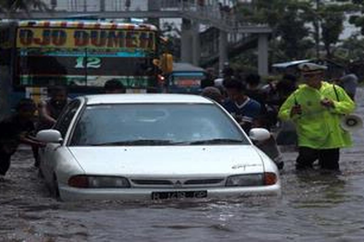 Warga mendorong mobil yang mogok saat menembus  genangan air di ruas Jalan Daan Mogot, tepatnya di depan Gedung Dinas pendapatan Daerah DKI Jakarta, Jakarta Barat, akibat meluapnya Saluran Mookervaart, Minggu (13/1/2013). Genangan air yang juga terjadi di sejumlah titik di sepanjang ruas jalan itu menyebabkan kemacetan dan kekacauan  lalu lintas.   