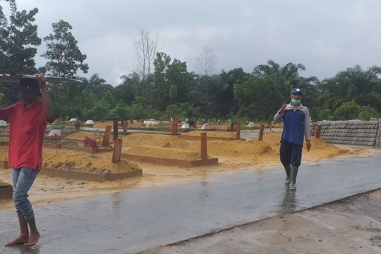 Subhan Zein (46) mencari tempat berteduh karena diguyur hujan saat merapikan makam korban Covid-19 di TPU Tengku Mahmud, Kelurahan Rumbai Bukit, Kecamatan Rumbai, Kota Pekanbaru, Riau, Sabtu (26/12/2020).