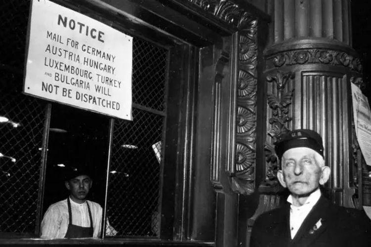 Dua pegawai di konter pos di bawah tanda yang mencantumkan layanan terbatas Eropa selama Perang Dunia Pertama di Cincinnati, Ohio, 1917.