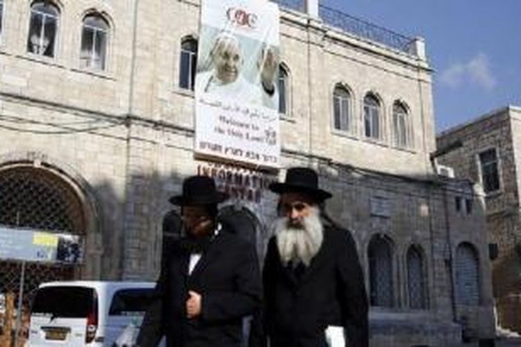 Dua orang Yahudi Ultra Ortodoks berjalan melewati sebuah poster besar foto Paus Fransiskus yang dipasang di fasad Christian Information Centre di Kota Tua Yerusalem. 
