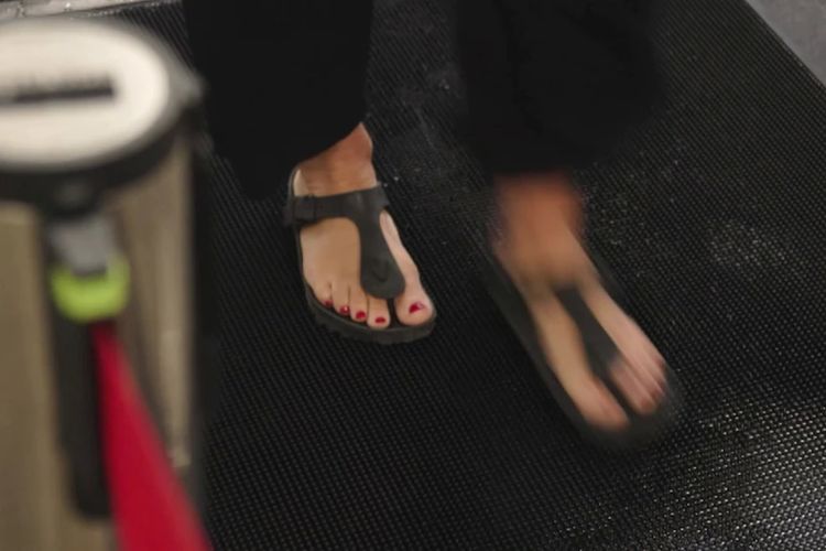 Seorang perempuan dengan alas kaki terbuka tidak memiliki masalah berjalan di atas keset di Bandara Perth.
