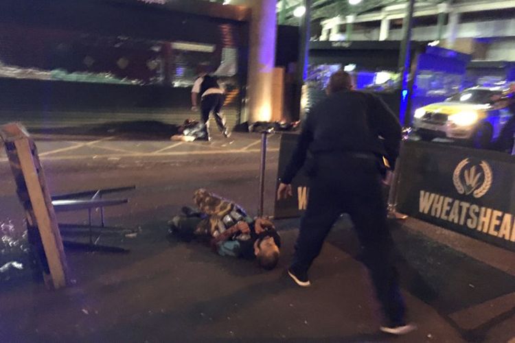 Polisi bersenjata berdiri di dekat terduga pelaku teror di Borough Market, London, Sabtu (3/6/2017).  Terduga pelaku tersebut yang terkapar mengenakan rompi dengan sejumlah tabung di dada. 