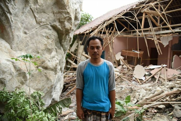 Dodi, warga Kampung Cihandeuleum, RT 009 RW 005, Desa Sukamulya, Kecamatan Tegalwaru, Kabupaten Purwakarta berdiri di dekat rumahnya yang rusak tertimpa batu.