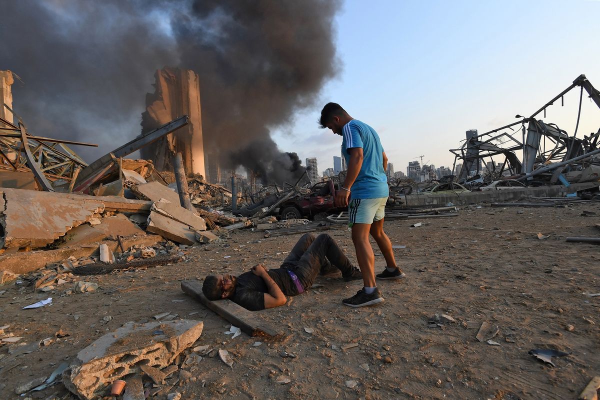 Seorang pria yang terluka terbaring di tanah dengan kepulan asap berada di depannya, dalam insiden ledakan yang menghantam ibu kota Lebanon, Beirut, pada 4 Agustus 2020. Petugas penyelamat mencari para korban pada 5 Agustus 2020 di tengah korban tewas yang melebihi 135 orang.
