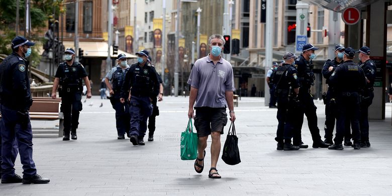 Seorang pria berjalan melewati petugas polisi yang berpatroli di jalan-jalan kawasan pusat bisnis Sydney pada 31 Juli 2021, ketika pihak berwenang memperingatkan terhadap protes anti-lockdown. 