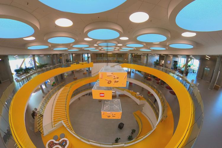 Pemandangan dari lantai III atrium Lego Campus, Kantor pusat Lego grup, di Kota Billund, Denmark. Interior areal ini menggunakan dominasi warna kuning dan putih, senada dengan logo Lego dan juga warna salah satu blok mainan Lego. Di setiap sisi dari selasar pada gedung tiga lantai ini, tersedia berbagai set sofa, dapur untuk membuat kopi dan teh, kafetaria, dan berbagai perlengkapan bermain. 