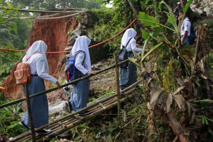 Sejumlah pelajar melintasi jembatan darurat dari arah utara menuju selatan dan sebaliknya di sisi jalur nasional yang tergerus longsor, Kecamatan Darma, Kabupaten Kuningan, Senin (20/2/2017). Setelah jalur nasional putus total, mereka berangkat sekolah lebih awal untuk mengejar waktu karena harus bergantian dan berhati-hati melintasi jembatan darurat. 