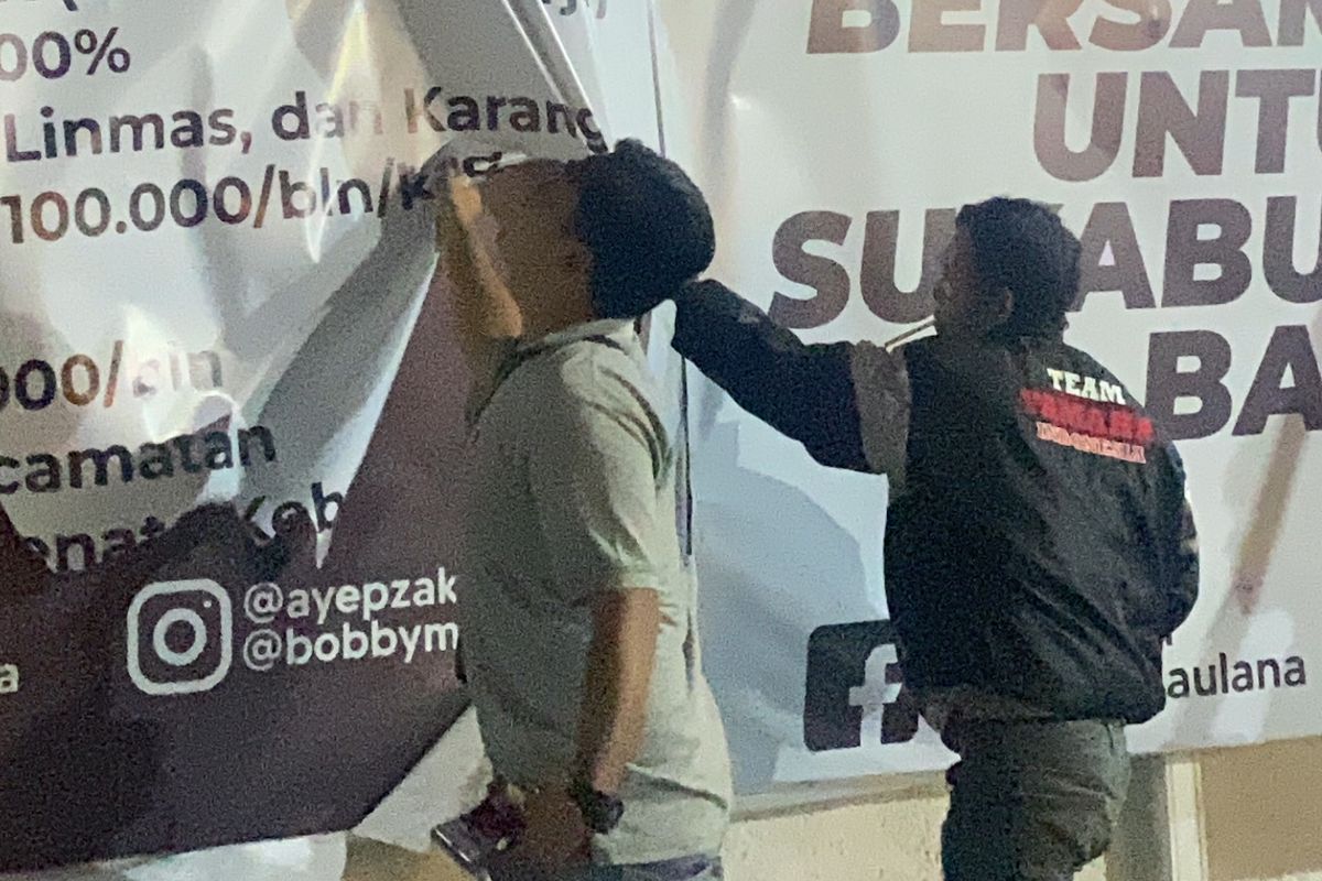 Dua orang tengah menertibkan baliho salah satu paslon wali kota - wakil wali kota yang masih terpampang di masa tenang. Selasa (26/11/2024) malam.