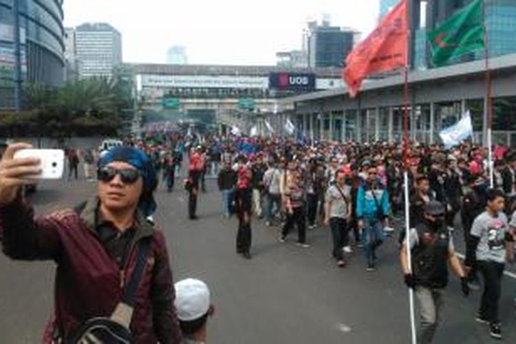 Seorang warga berfoto dengan latar belakang massa buruh yang berjalan menuju Bunderan Hotel Indonesia, Jakarta Pusat, Jumat (1/5/2015).