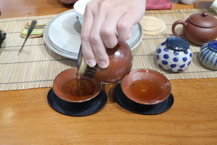 Proses penuangan teh yang baru selesai diseduh ke dalam gelas saji.