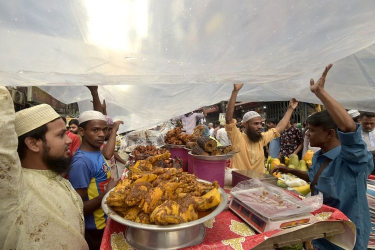Stan makanan berbuka menggunakan plastik untuk melindungi dagangan dari hujan di pasar Chawkbazar yang berlangsung saat Ramadhan di Dhakaz Bangladesh.