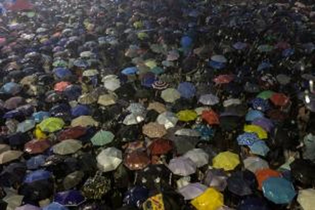 Para pengunjuk rasa pro-demokrasi menggunakan payung untuk menahan guyuran hujan saat mereka melakukan aksi duduk di pusat pemerintahan Hongkong mengecam sistem pemilihan pemimpin baru kota itu yang dinilai tidak demokratis.