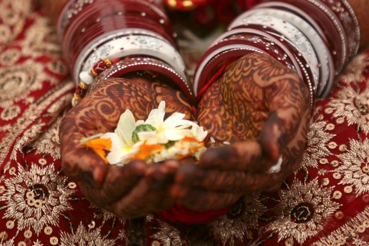 Seorang pengantin wanita memegang bunga dengan tangannya yang dihiasi dengan pasta pacar selama upacara pernikahannya di kota Ahmedabad, India barat.