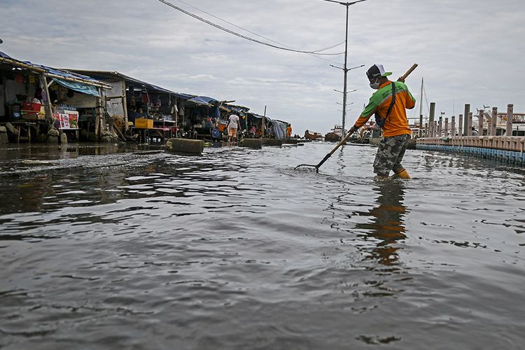 Petugas kebersihan membersihkan sampah saat banjir rob di Pelabuhan Kali Adem, Muara Angke, Jakarta, Jumat (1/1/2021). Banjir yang terjadi sejak Kamis (31/12/2020) itu dikarenakan pasang surut air laut.