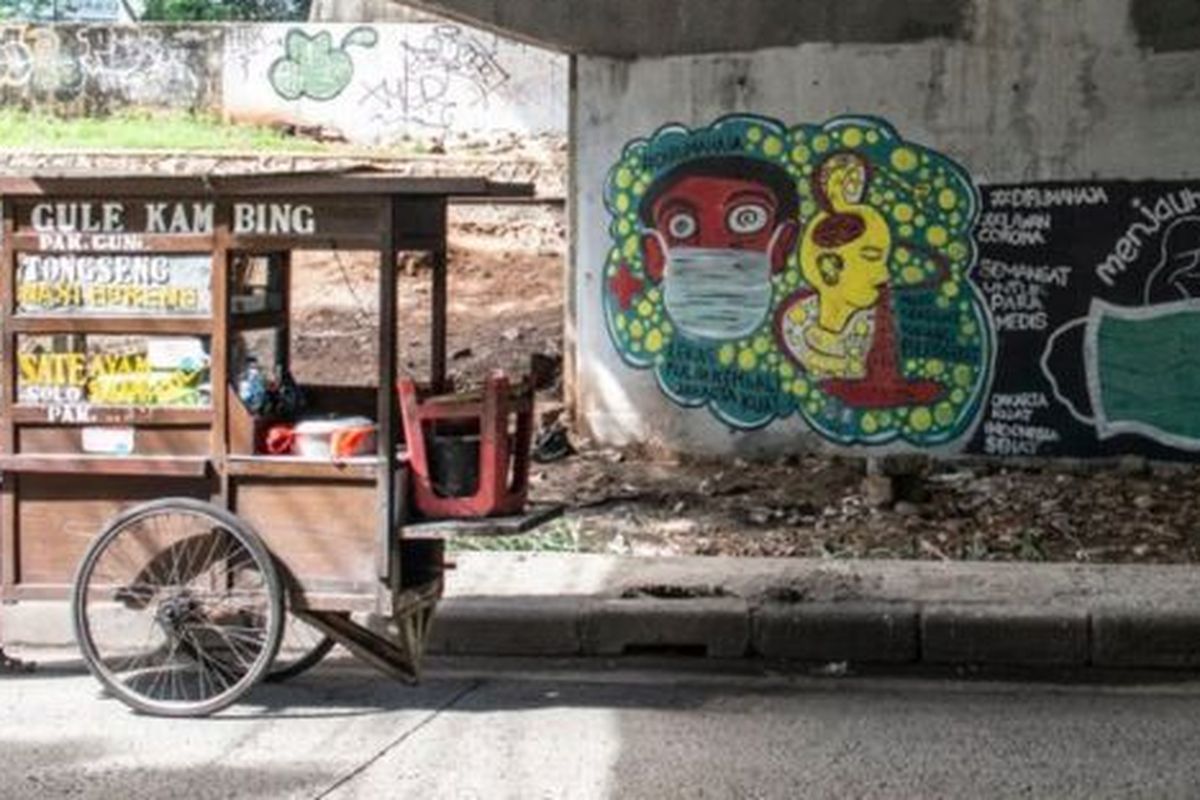 Pedagang kaki lima berjalan di dekat mural bertema pencegahaan penyebaran virus Corona atau COVID-19 di Jakarta, Rabu (01/04) 