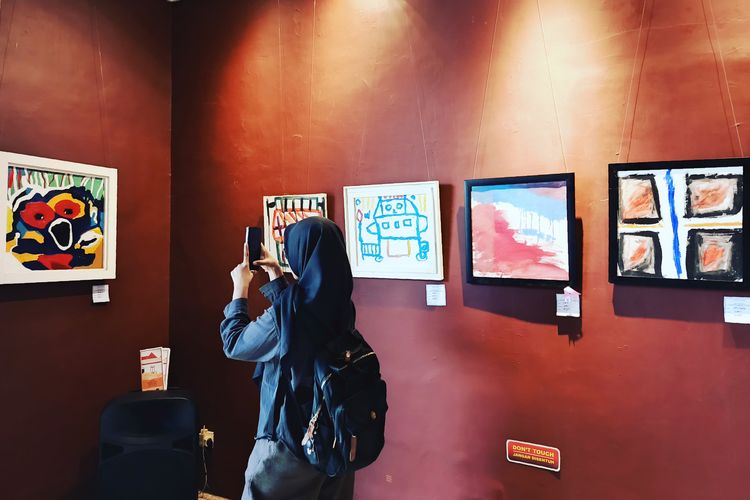 Seorang pengunjung sedang mendapkumentasikan hasil karya lukisan dua pelukis cilik down syndrome di Galeri Merah utih Balai Pemuda Surabaya yang berlangsung mulai tanggal 14-20 Juni 2025.