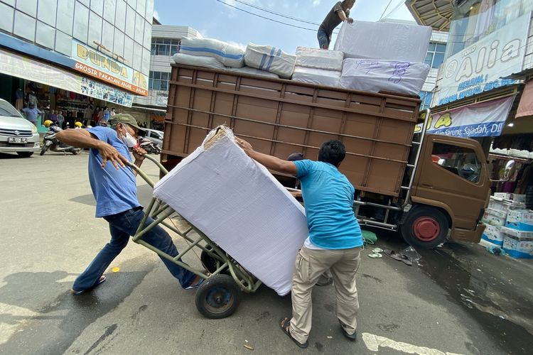 Para buruh panggul di Pasar Tengah saling membantu rekannya mengangkut muatan karung berisi sekitar 100 kilogram pakaian ke atas lori, Rabu (15/3/2023).