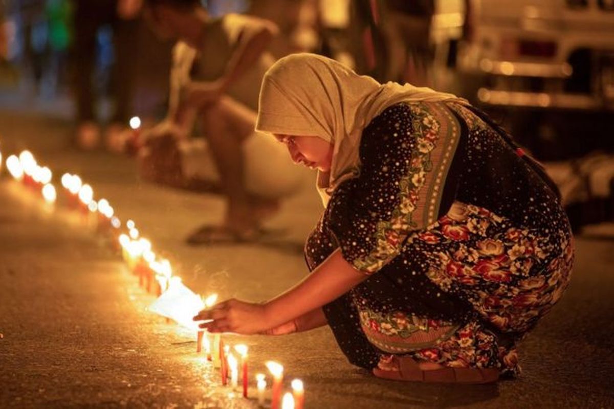 A woman wearing a headscarf light a candle in Myanmar in tribute to protesters who died in March 2021.  