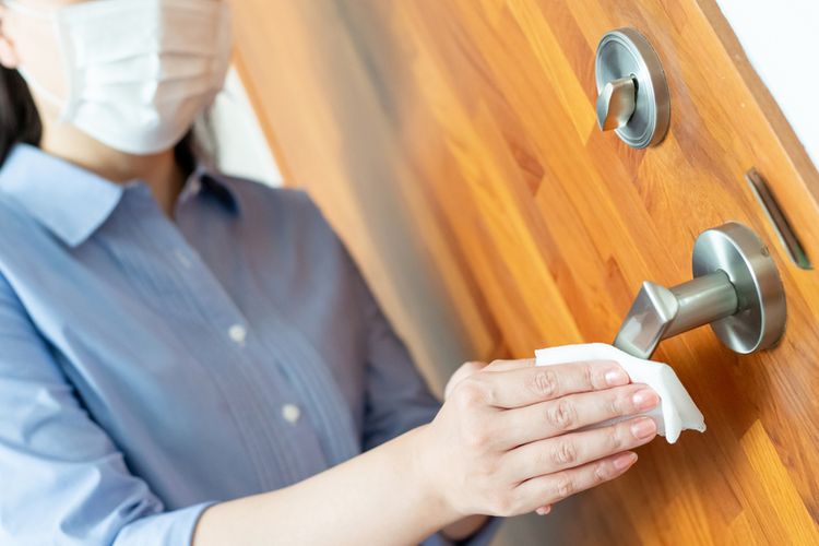Seorang wanita membersihkan gagang pintu untuk mencegah infeksi virus corona