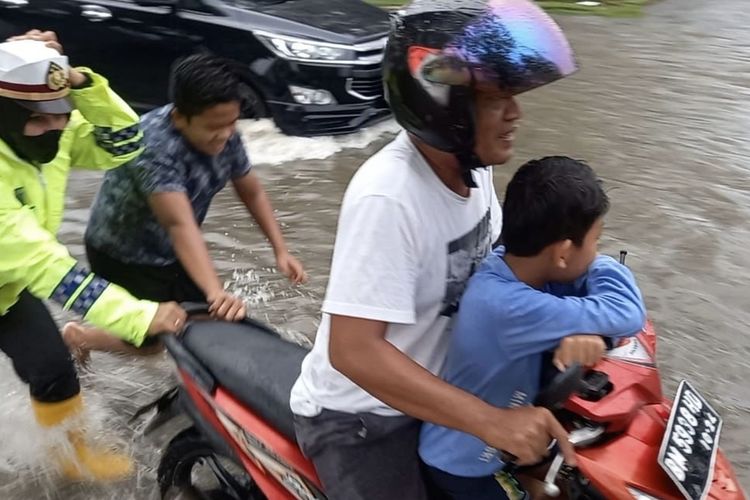 Seorang Polwan AKP Akira, dorong motor warga yang mogok akibat banjir di Jalan Sultan Syarif Kasim Kota Dumai, Riau. Rabu (27/10/2021).