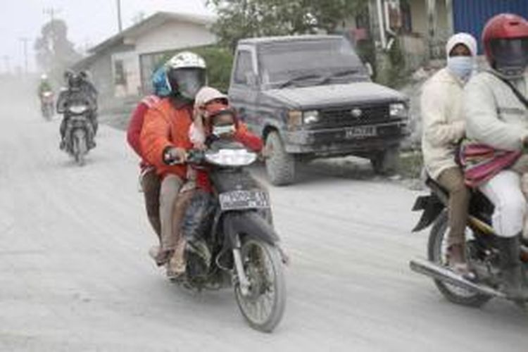 Warga melintasi jalan yang tertutup abu vulkanik letusan Gunung Sinabungdi Karo, Sumut, 15 September 2013.  Letusan gunung yang terjadi Minggu pukul 02.51, mengakibatkan ribuan orang dari belasan desa di kaki gunung terpaksa diungsikan.