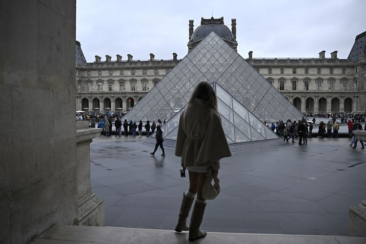 Seorang perempuan mengamati antrean pengunjung yang hendak memasuki piramida Museum Louvre di Paris, Perancis, sesaat sebelum pengumuman bahwa lokasi ini tetap ditutup untuk hari kedua pada 20 Oktober 2025, setelah terjadi perampokan.