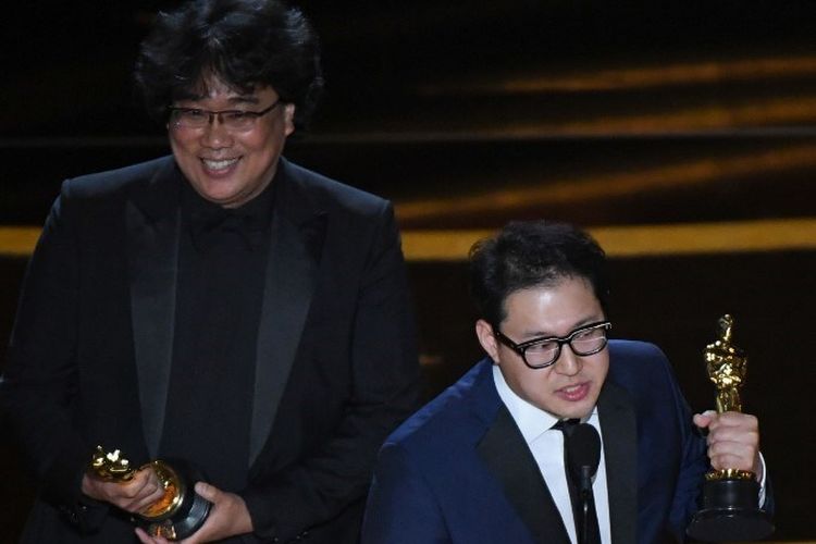 Penulis skenario Han Jin-won (kanan) dan sutradara Bong Joon Ho memberi sambutan setelah mereka meraih Oscar naskah asli terbaik untuk film Parasite pada perhelatan Academy Awards 2020 di Dolby Theatre, Hollywood, California, Minggu (9/2/2020).