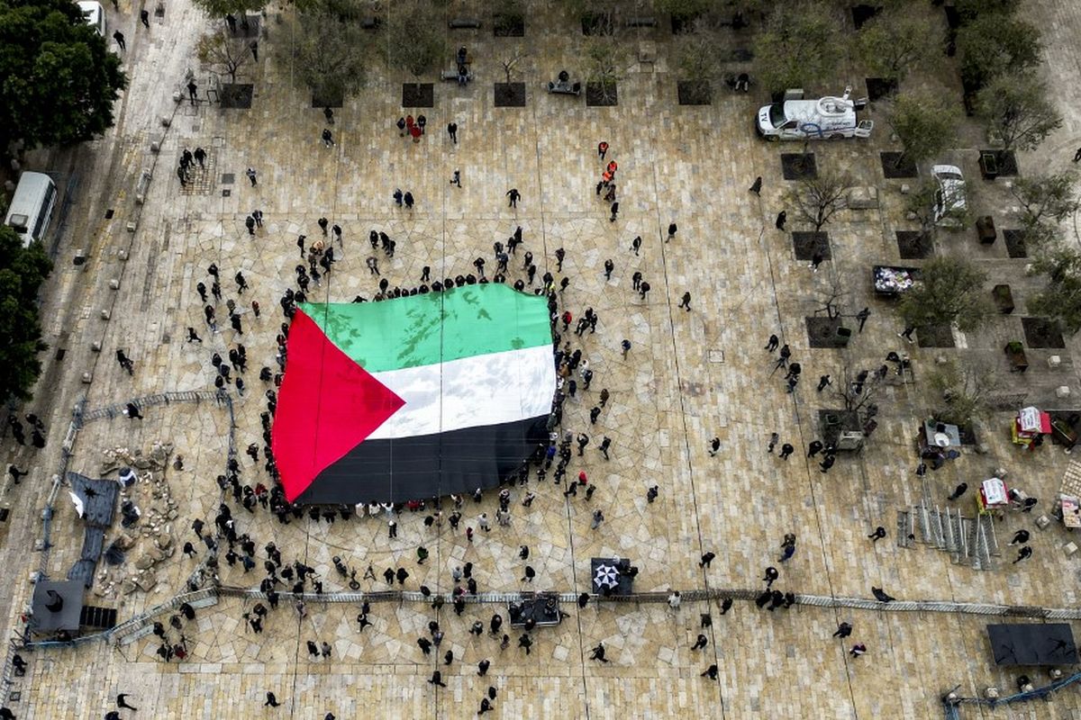 Foto udara ini menunjukkan para pengunjung yang membentangkan bendera Palestina raksasa saat mereka berkumpul di Alun-Alun Palungan di luar Gereja Kelahiran di kota alkitabiah Bethlehem di Tepi Barat yang diduduki pada Malam Natal (menurut tradisi Barat) pada 24 Desember 2023.