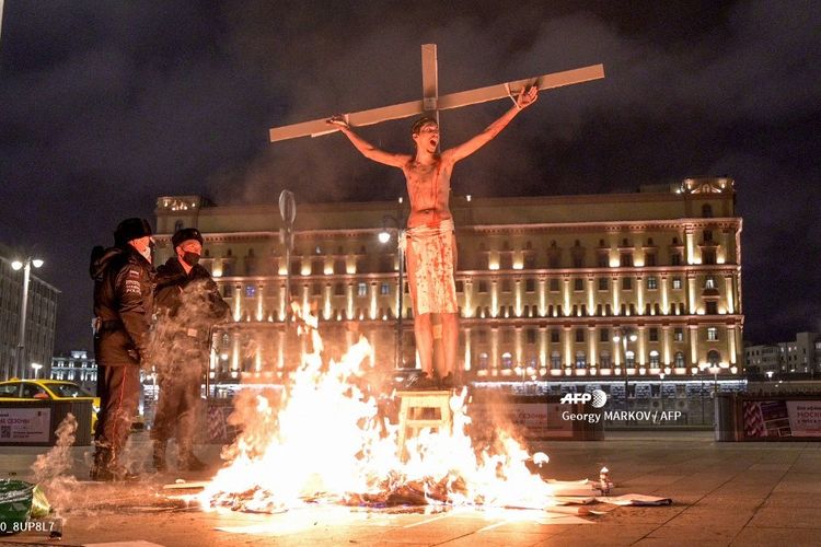 Dua polisi melihat pria setengah telanjang, yang merupakan aktivis politik Pavel Krisevich, yang berdiri disalibkan dengan api menyala di depannya di Lapangan Lubyanka, Moskwa, Rusia, pada 5 November 2020. Dia kemudian dipenjara selama 15 hari.