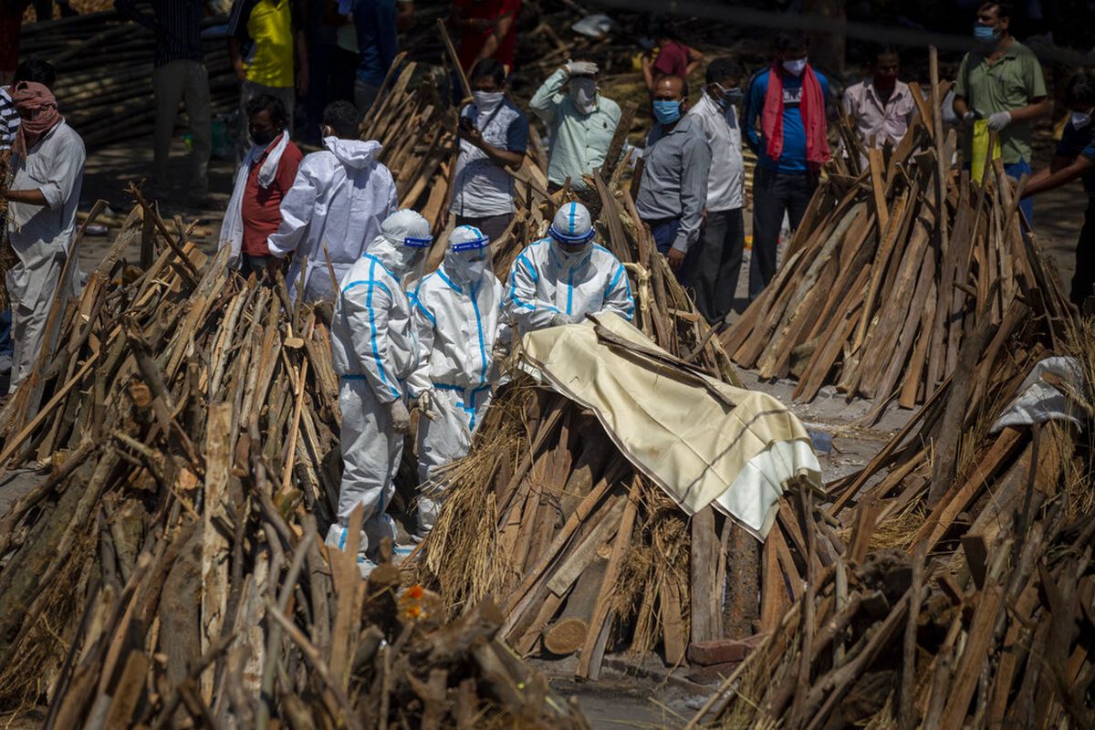Orang-orang melakukan ritual di samping tumpukan kayu pemakaman anggota keluarga yang meninggal karena Covid-19 di tanah yang telah diubah menjadi krematorium kremasi massal korban Covid-19 di New Delhi, India, Sabtu, 24 April 2021.