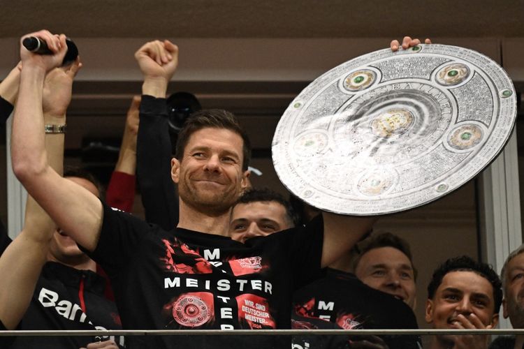 Bayer Leverkusen membungkus gelar juara Bundesliga 2023-2024 dengan pesta gol 5-0 ke gawang Werder Bremen pada Minggu (14/4/2024). Pelatih Xabi Alonso berpose dengan trofi juara Liga Jerman usai laga tersebut.