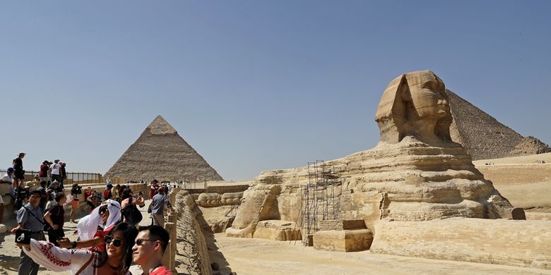 Wisatawan berfoto dengan latar belakang patung Spink dan piramida di Mesir.