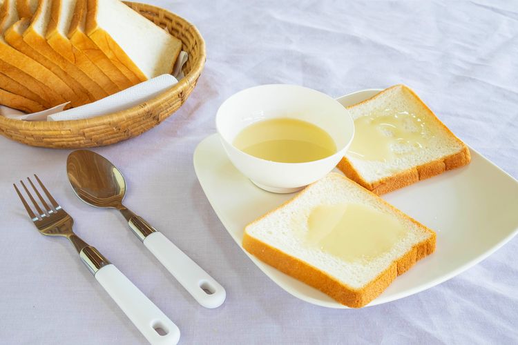 Ilustrasi sarapan dengan roti tawar dan topping susu kental manis.
