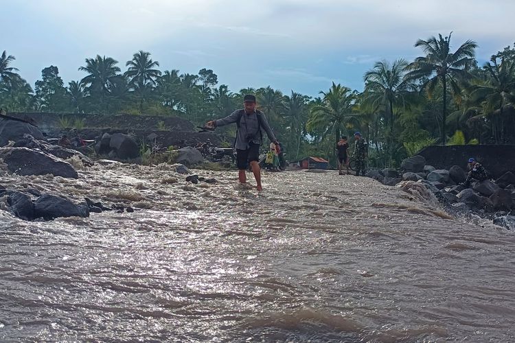 Warga melintasi sisa banjir lahar hujan Gunung Semeru di Sungai Regoyo, Sabtu (28/6/2025)
